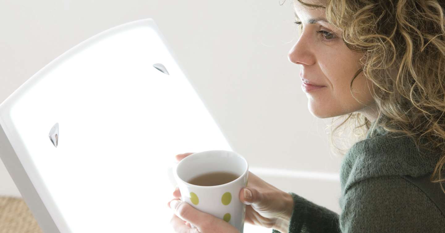 a woman drinking coffee near her sun lamp or light box to help with seasonal affective disorder