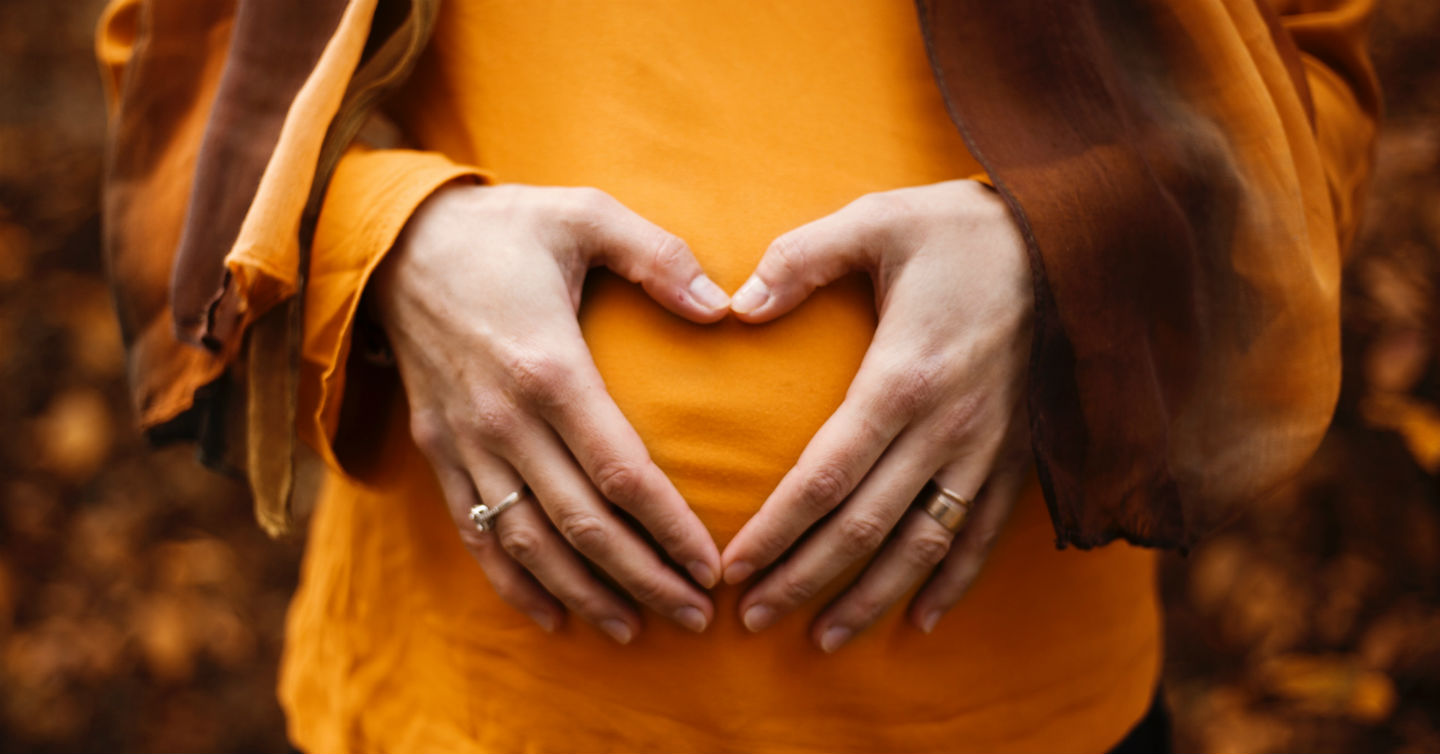 woman making heart symbol with hands over pregnant belly