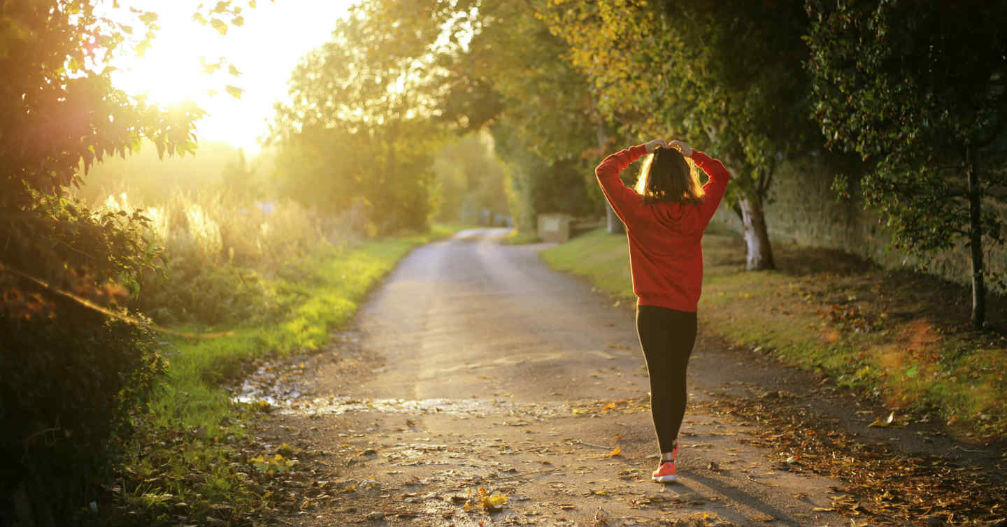 woman holding head walking on a path in the woods