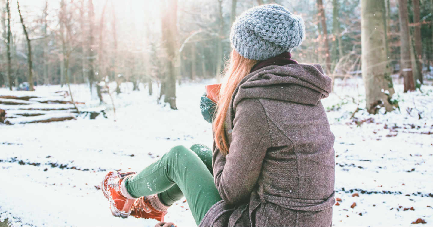 person sitting in snow drinking a hot beverage