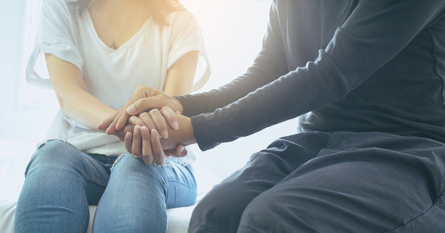 person comforting another sitting down with sunlight behind them