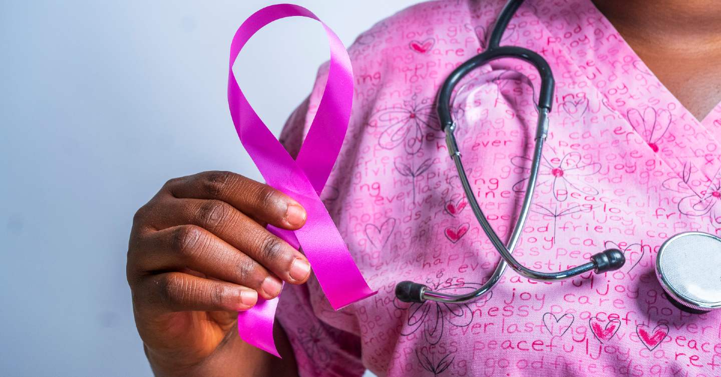 woman holding pink breast cancer ribbon in front of stethoscope