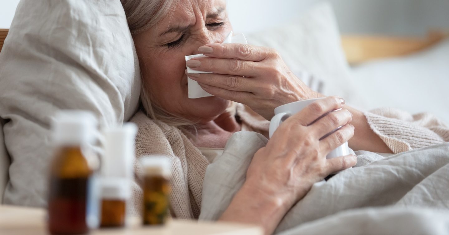 woman coughing with bottles of pills next to bed