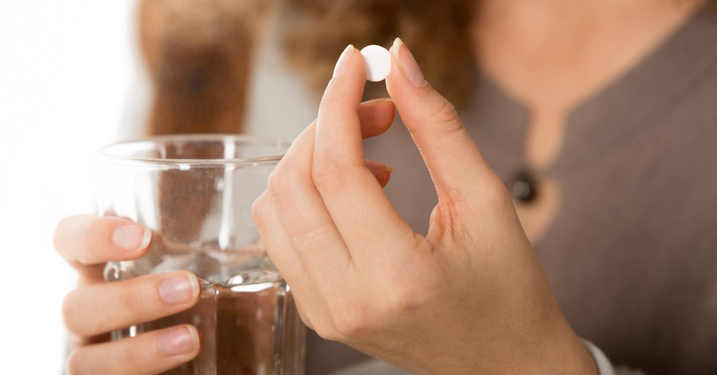 person holding a glass of water and a pill