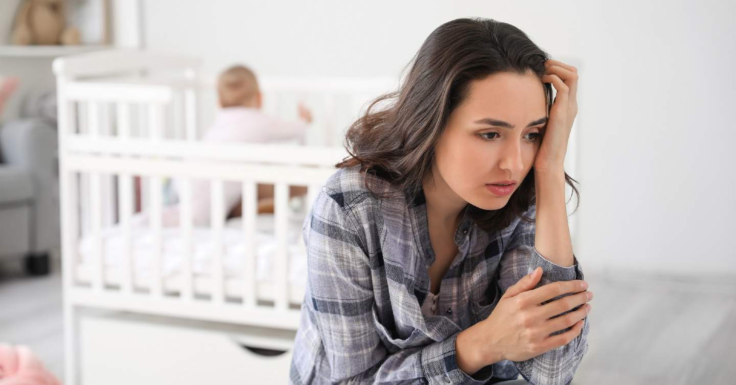 woman looking sad in front of crib with postpartum depression